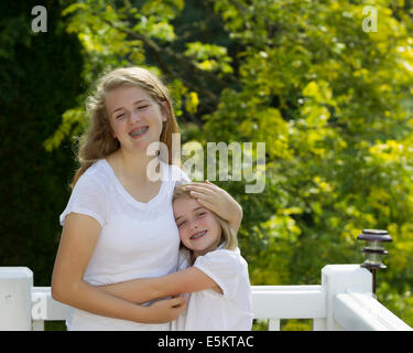 Vue de face de deux soeurs serrant les uns les autres tandis que l'extérieur sur terrasse avec des arbres en arrière-plan flou Banque D'Images