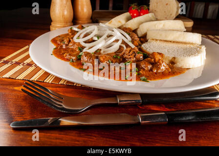 République tchèque traditionnel goulasch avec boulette panée et l'oignon sur plaque blanche sur table en bois Banque D'Images