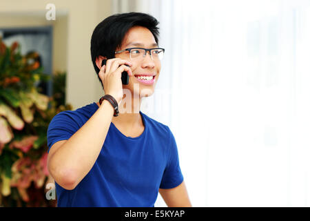 Smiling Asian man talking on the phone at home Banque D'Images