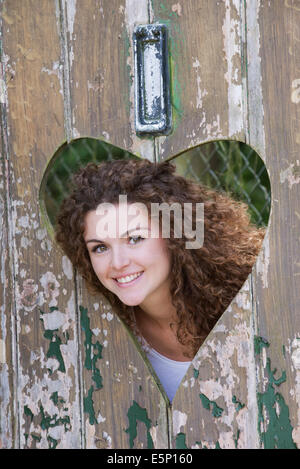 Adolescent à la recherche par forme de coeur découpe dans une vieille porte Banque D'Images