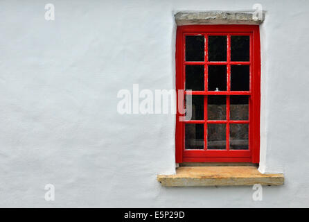 Petite fenêtre à guillotine peint rouge avec linteau et cill en pierre situé dans le mur peint en blanc d'un cottage traditionnel irlandais. Banque D'Images