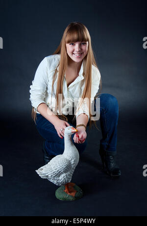 Belle jeune fille de race blanche avec de longs cheveux blonds portant veste blanche et bleu jeans et feedenig l'oie artificiel Banque D'Images