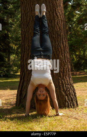 Une jolie fille aux cheveux rouge effectue une main contre un arbre Banque D'Images