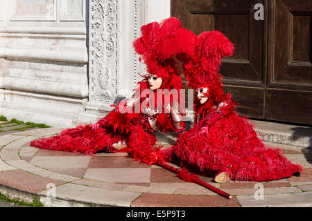 Paire de femmes dans des costumes à plumes rouge repose dans la partie avant de la trappe de l'église San Zaccaria pendant le carnaval de Venise. Banque D'Images