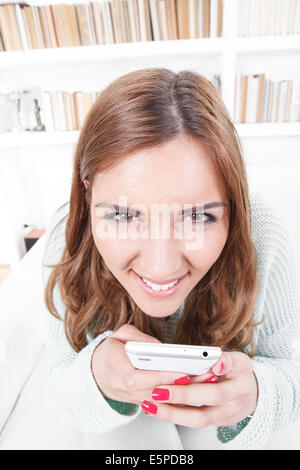 Jeune femme avec expression visage fou essaie de dépit insidieusement avec un téléphone mobile via un message ou appeler à son domicile, liv Banque D'Images