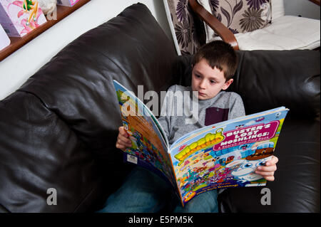 Boy reading Moshi Monsters livre sur canapé Banque D'Images