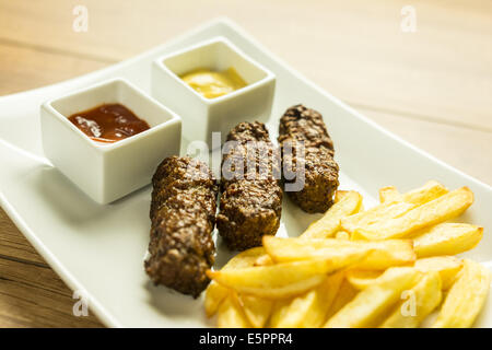 Boulettes de nourriture traditionnelle roumaine Mici et de frites avec du ketchup et de la moutarde Banque D'Images