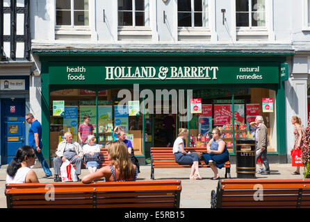 Les gens assis à l'extérieur a Holland & Barrett shop à Shrewsbury, Shropshire, England, UK Banque D'Images