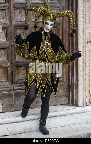 Jester ou clown en costume noir et or, en face de l'église San Zaccaria pendant le carnaval de Venise. Banque D'Images