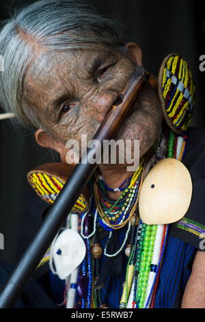 85-ans femme Chin (Yun) Eian jouer flûte, l'État de Chin, Mindat, Myanmar. Son visage est tatoué, traditionnelles chez les Chin Banque D'Images