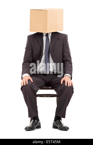 L'homme en costume noir assis sur une chaise en bois avec une boîte en carton sur la tête Banque D'Images