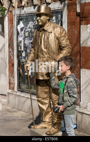 Jeune garçon se tient avec golden statue vivante street performer pendant le carnaval de Venise. Banque D'Images