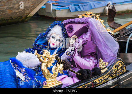 Les femmes dans des costumes bleus et violets à une télécabine vers le bas un canal latéral pendant le carnaval de Venise. Banque D'Images