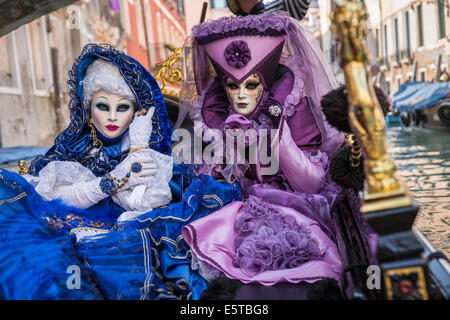 Les femmes dans des costumes bleus et violets à une télécabine vers le bas un canal latéral pendant le carnaval de Venise. Banque D'Images