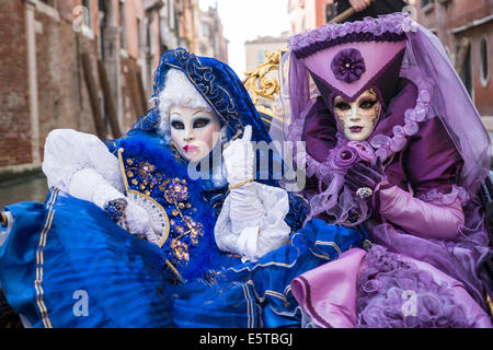 Les femmes dans des costumes bleus et violets à une télécabine vers le bas un canal latéral pendant le carnaval de Venise. Banque D'Images