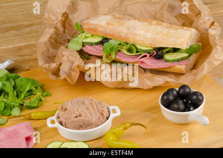 Baguette méditerranéen avec des ingrédients sur planche à découper en bois Banque D'Images