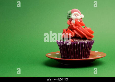 Cupcake de Noël en violet à pois avec enrubanneuse glaçage rouge et décoration festive Santa contre un fond vert Banque D'Images