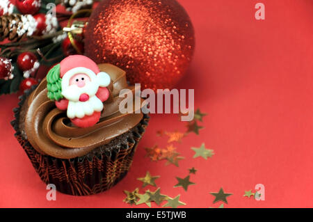 Petits gâteaux au chocolat de Noël avec le père Noël fait face à l'encontre d'un contexte festif rouge. Banque D'Images