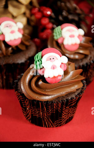 Petits gâteaux au chocolat de Noël avec le père Noël fait face à l'encontre d'un contexte festif rouge. Banque D'Images