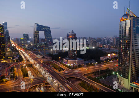 Belle vue panoramique sur la ville de la capitale chinoise et le célèbre monument du siège de CCTV, avec les lumières de la circulation sur le troisième périphérique et les bureaux et les bâtiments éclairant la scène en début de soirée. Rare scène panoramique pendant l'heure bleue juste après le coucher du soleil avec un ciel clair à Guomao, le quartier central des affaires de Beijing, situé dans le quartier de Chaoyang, Chine, RPC. © Olli Geibel Banque D'Images