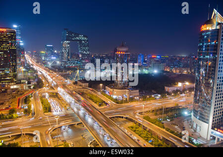 Belle vue panoramique sur la ville de la capitale chinoise et le célèbre monument du siège de CCTV, avec les lumières de la circulation sur le troisième périphérique et les bureaux et les bâtiments éclairant la scène en début de soirée. Rare scène panoramique pendant l'heure bleue juste après le coucher du soleil avec un ciel clair à Guomao, le quartier central des affaires de Beijing, situé dans le quartier de Chaoyang, Chine, RPC. © Olli Geibel Banque D'Images