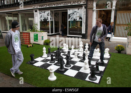 Les jeunes hommes jouent aux échecs sur un plateau d'échecs géant dans la rue posée sur gazon artificiel.Manchester, Royaume-Uni 6 août 2014.DIG The City Deansgate, un festival annuel de jardinage urbain organisé par le Business Improvement District de Manchester – BID. Banque D'Images