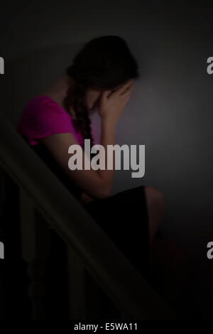 Moody shot d'une jeune femme assise seule dans le noir, avec sa main sur son visage. La dépression et d'humeur. Banque D'Images