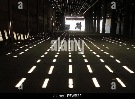 Santa Monica, Californie, USA. 6e août, 2014. Un couple passe par une passerelle sous la jetée de Santa Monica comme flux de lumière à travers les ouvertures dans les panneaux de bois. © Jonathan Alcorn/ZUMA/Alamy Fil Live News Banque D'Images