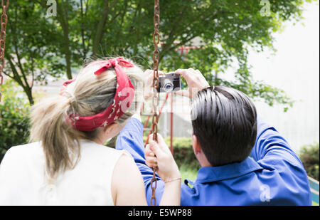 Vue arrière du jeune couple vintage avec caméra dans jardin selfies Banque D'Images