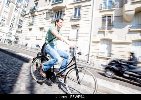 Mid adult male cyclist accélérer vers le bas de la rue pavée, Paris, France Banque D'Images
