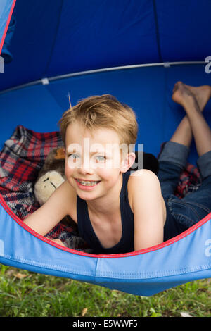 Portrait of smiling boy lying en tente suspendue au-dessus de l'herbe Banque D'Images