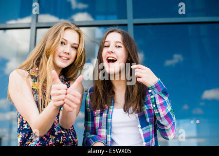 Portrait de deux jeunes femmes faire Thumbs up en face de bureau en verre Banque D'Images