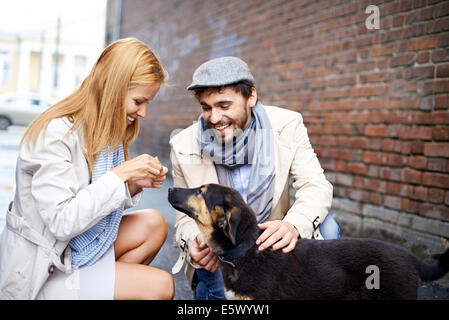 Portrait of happy young couple in vêtement élégant chien d'alimentation à l'extérieur Banque D'Images