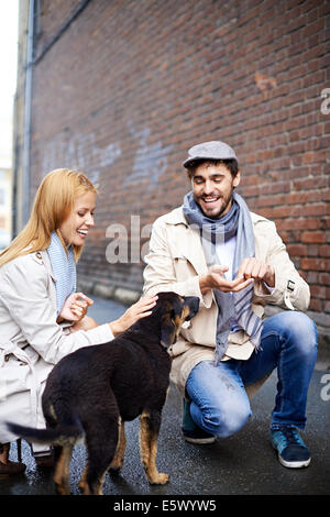 Portrait of happy young couple in vêtement élégant chien d'alimentation à l'extérieur Banque D'Images