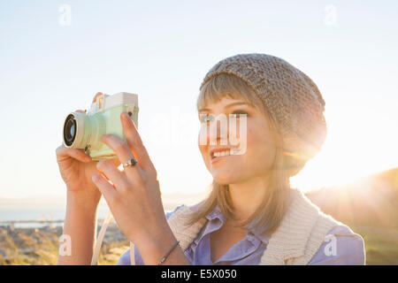 Young woman taking photograph avec l'appareil photo au coucher du soleil Banque D'Images