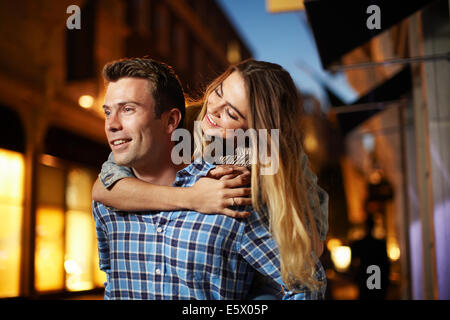 Couple giving piggy back on city street at night Banque D'Images