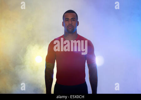 Studio portrait of muscular young sportsman dans spots et mist Banque D'Images