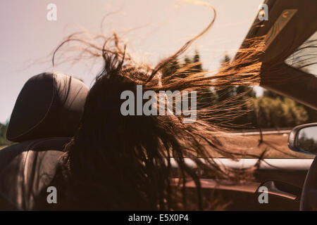 Mid adult woman driving red cabriolet avec de longs cheveux blowing in wind Banque D'Images