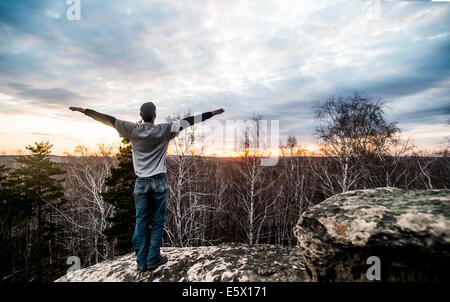 Jeune homme avec les bras tendus au-dessus de rock formation au coucher du soleil Banque D'Images