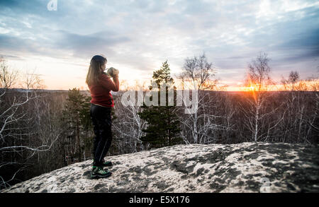 Young woman on top rock photographier le coucher du soleil Banque D'Images