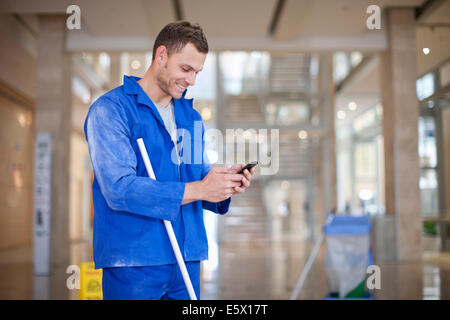 Nettoyant mâle texting on smartphone in office atrium Banque D'Images