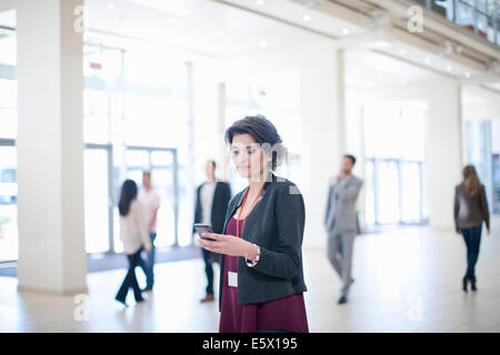 Young businesswoman texting on smartphone dans le corridor du centre de conférence Banque D'Images