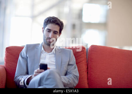 Young businessman texting on smartphone canapé dans conference centre Banque D'Images