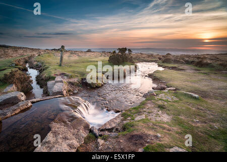 Coucher du soleil à Windy Publiez une ancienne croix de granit aux côtés le Beckamoor Brook comme il traverse le Sortridge Grimstone et L Banque D'Images