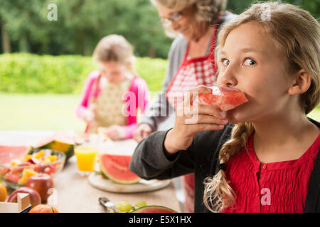 Jeune fille espiègle à patio table eating watermelon slice Banque D'Images