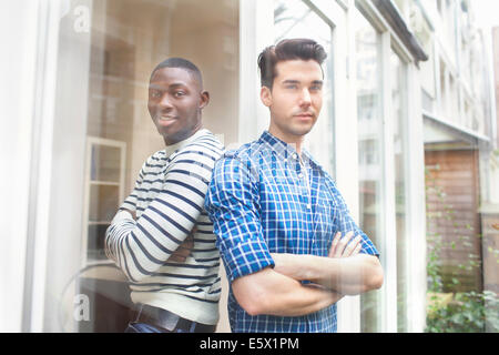 Portrait de deux jeunes hommes dos à dos dans jardin Banque D'Images