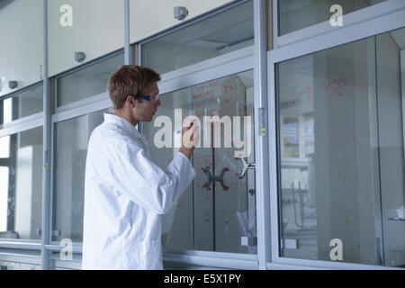 Jeune homme d'écriture scientifique résultats sur fenêtre hotte Banque D'Images