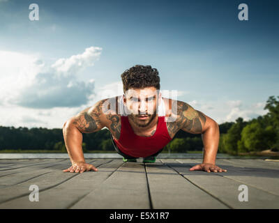 Niveau Surface portrait of young man doing push ups on lake pier Banque D'Images