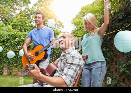 Les amis masculins playing acoustic guitar in garden et young woman dancing Banque D'Images