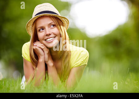 Happy girl in hat lying in grass in park Banque D'Images